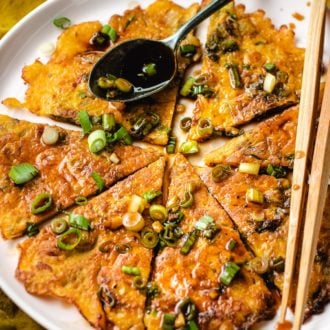 Sliced kimchi jeon drizzled with pancake sauce served on a big round plate