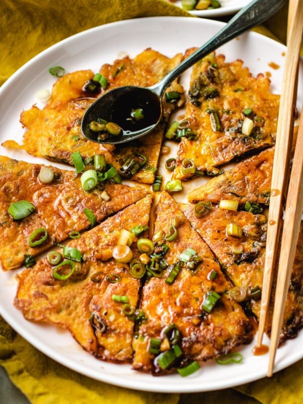 Sliced kimchi jeon drizzled with pancake sauce served on a big round plate