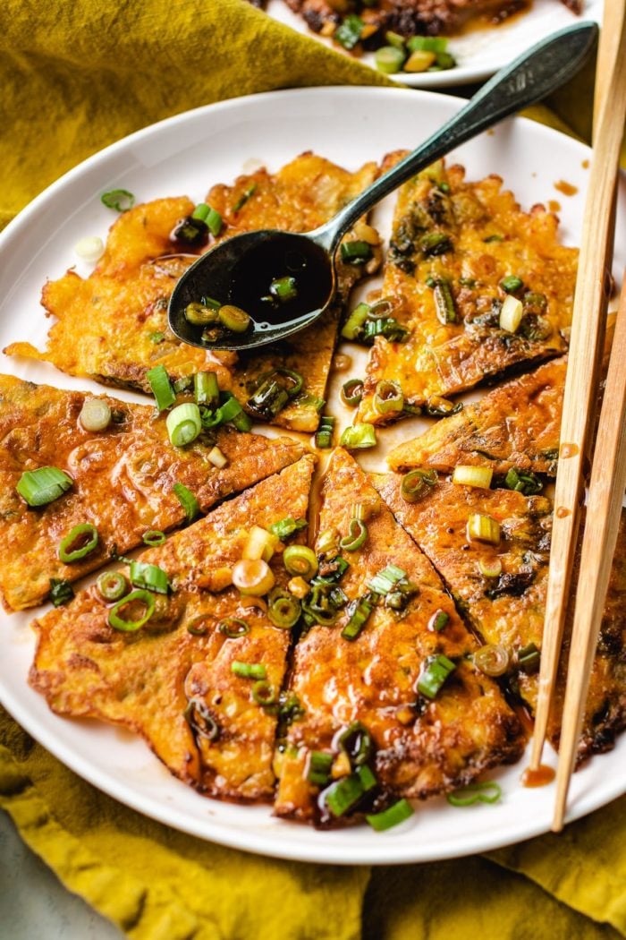 Sliced kimchi jeon drizzled with pancake sauce served on a big round plate