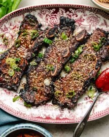 Photo shows LA galbi (korean short ribs) barbequed and served on a big white plate with side dishes on the side.