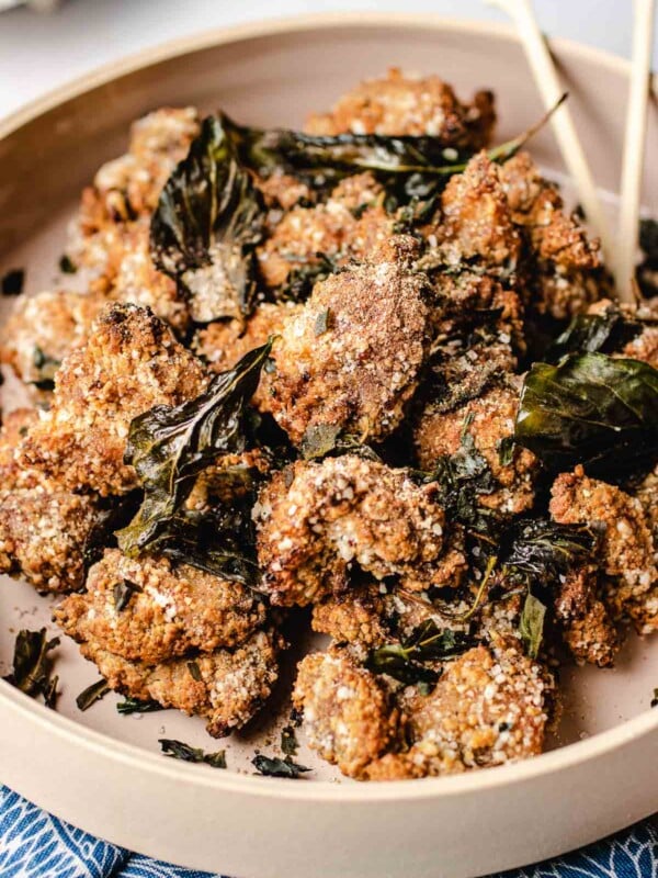 A close shot shows crispy crunchy Taiwanese popcorn chicken with crushed basil leaves served in a light pink big plate.