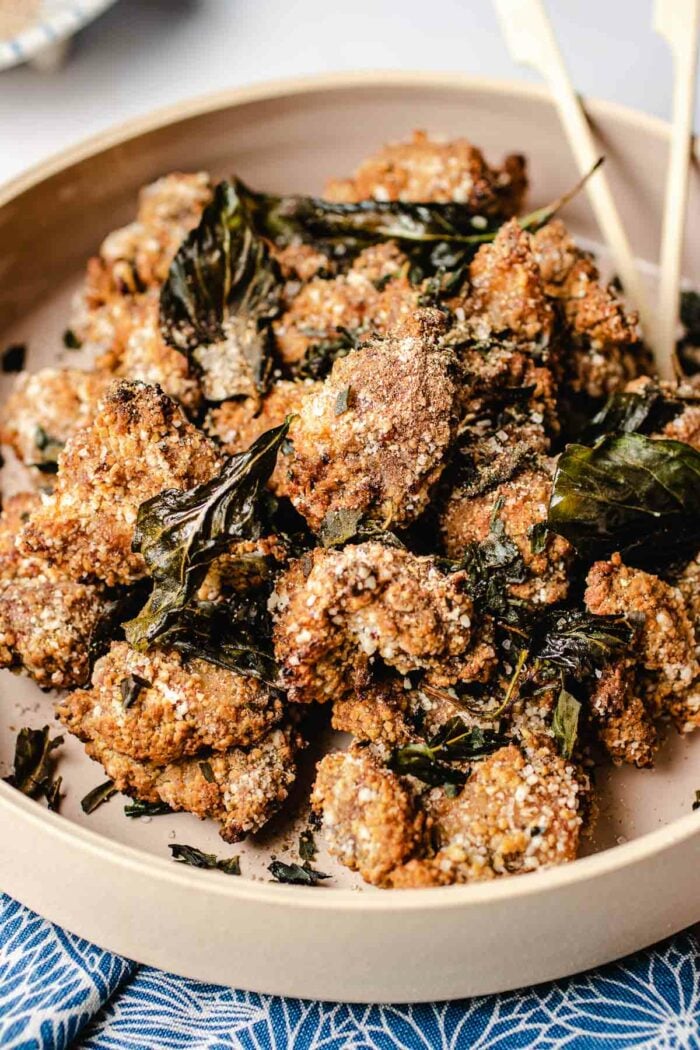 A close shot shows crispy crunchy Taiwanese popcorn chicken with crushed basil leaves served in a light pink big plate.