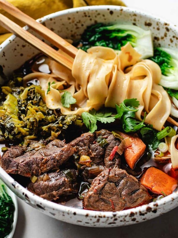 Feature image shows a big bowl of Taiwanese beef noodle soup served with bok choy and pickled mustard greens in the bowl with chopsticks.