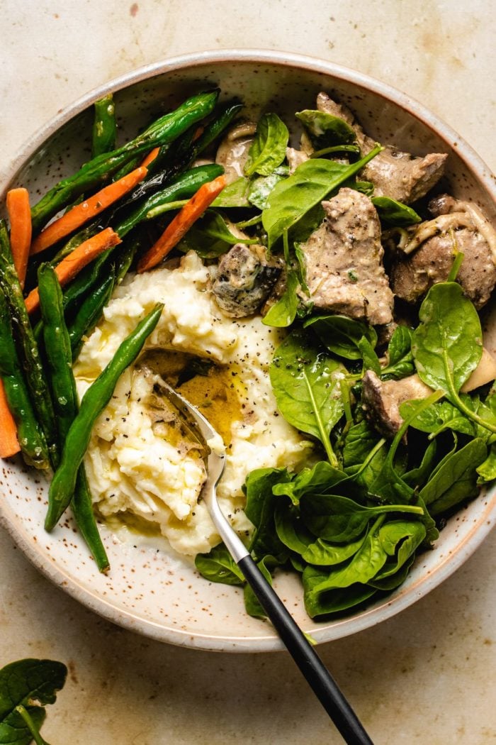 A serving platter with boneless leg of lamb stew recipe, mashed potatoes, and green beans