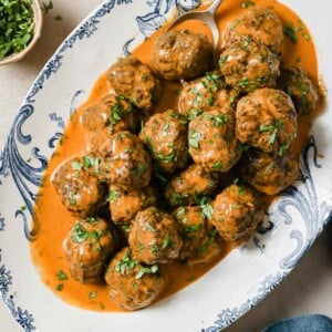 Feature image shows baked Thai red curry meatballs with curry sauce served in a blue white color plate.