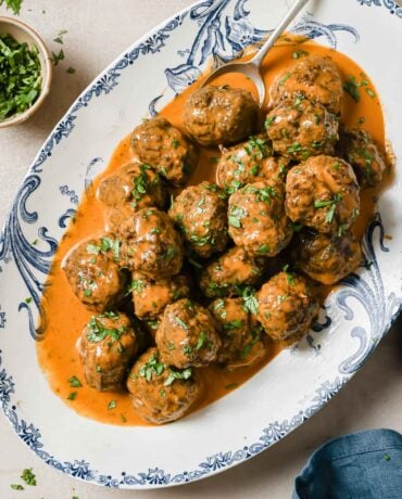 Feature image shows baked Thai red curry meatballs with curry sauce served in a blue white color plate.