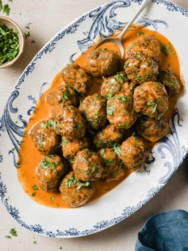 Feature image shows baked Thai red curry meatballs with curry sauce served in a blue white color plate.