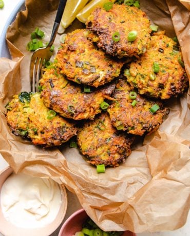 Photo shows 6 pan fried zucchini fritters served on a plate with sour cream and scallions on the side