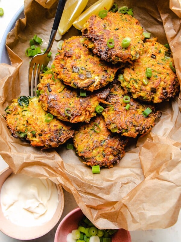 Photo shows 6 pan fried zucchini fritters served on a plate with sour cream and scallions on the side