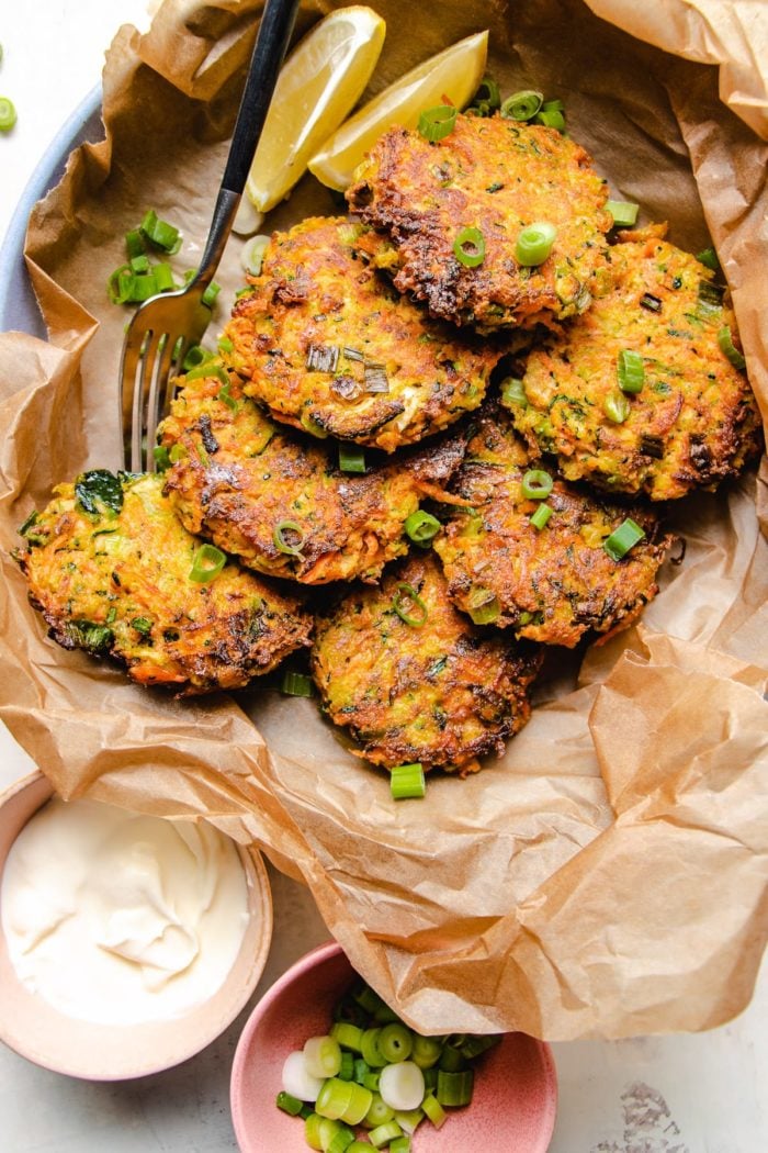 Photo shows 6 pan fried zucchini fritters served on a plate with sour cream and scallions on the side