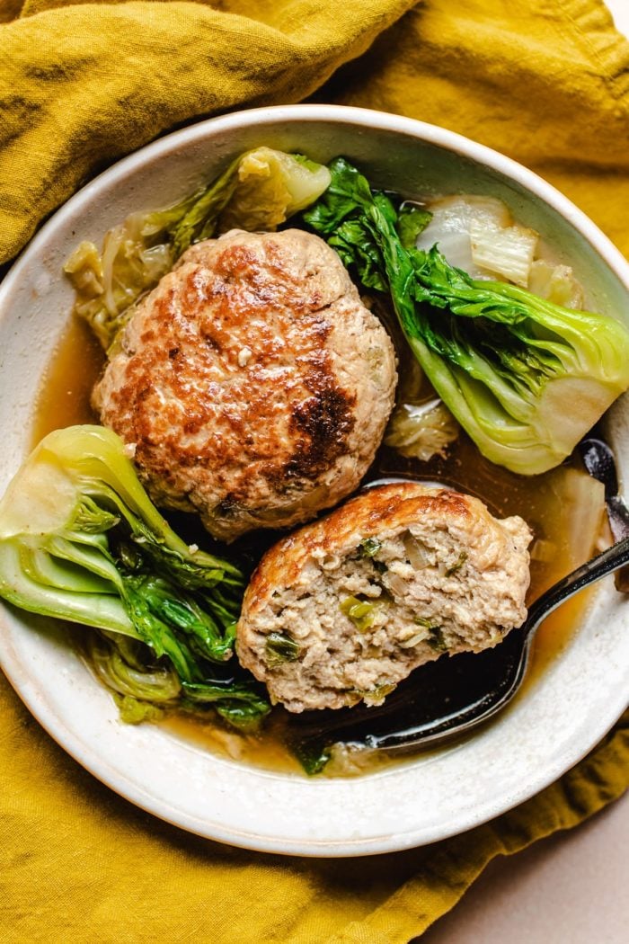 A close shot shows two lion's head meatballs with bok choy and cabbage served in a small white bowl