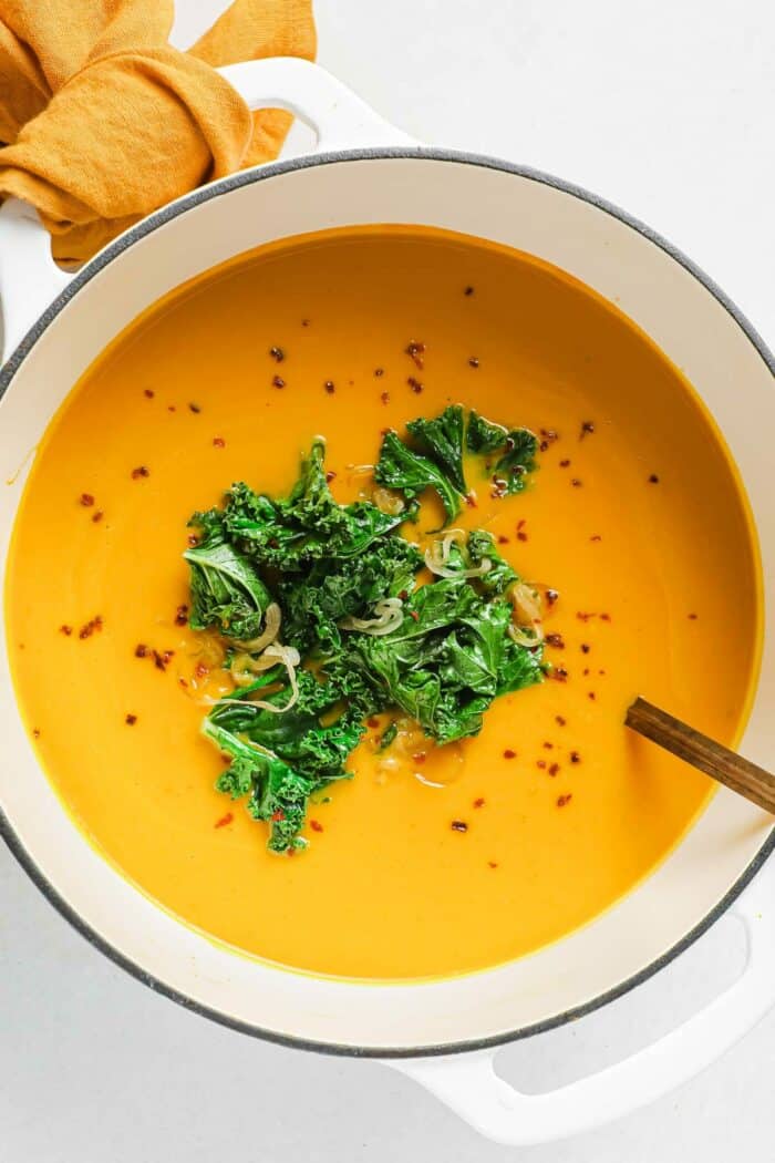 Creamy kabocha squash soup blended and made in a Dutch oven with sauteed kale on top.