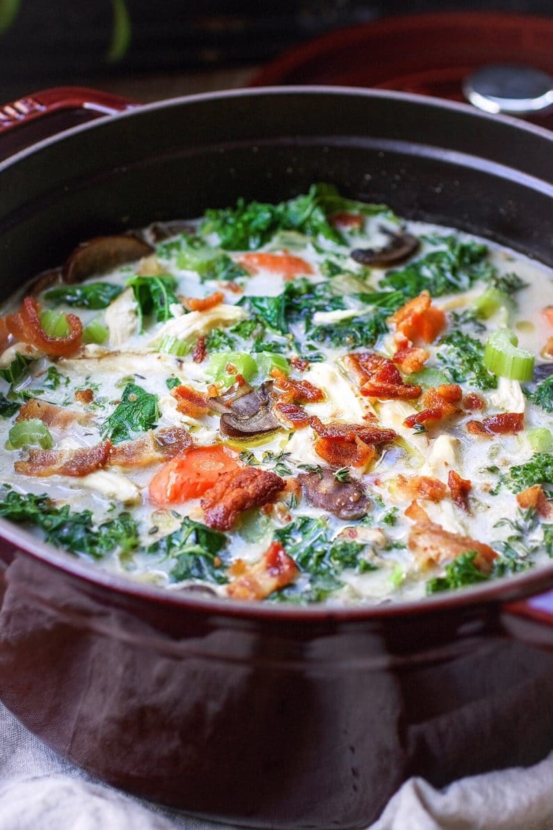 A side shot image shows a large pot of creamy chicken and kale soup with bacon crumbles on top in a Dutch oven.