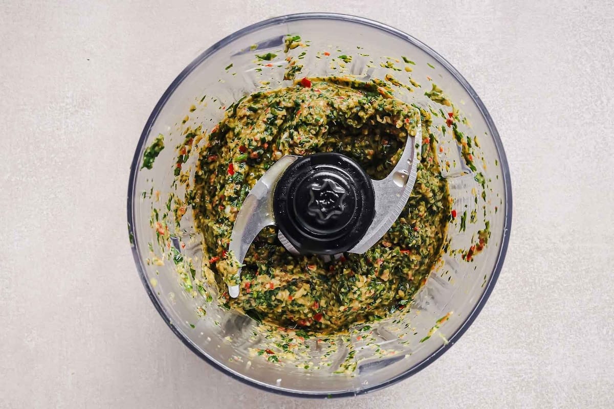 Top view of a food processor bowl with a vibrant green and yellow paste, made from herbs and spices—perfect for seasoning your Whole chicken Dutch oven recipe before roasting to golden perfection.