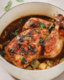 An image shows whole roasted chicken inside of a Dutch oven with vegetables in the pot.