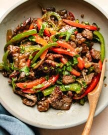 A close shot photo shows sliced and marinated beef stir fry with onions and peppers served in a light color plate.