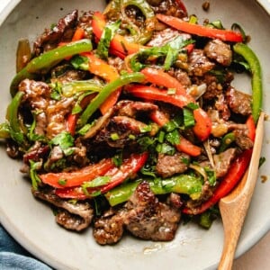 A close shot photo shows sliced and marinated beef stir fry with onions and peppers served in a light color plate.