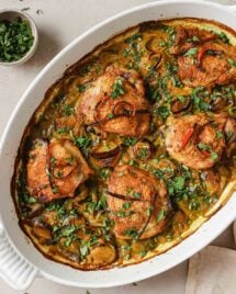 Image shows baked turmeric chicken thighs with leeks in a white casserole dish with dairy-free cream sauce.