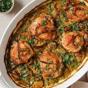 Image shows baked turmeric chicken thighs with leeks in a white casserole dish with dairy-free cream sauce.