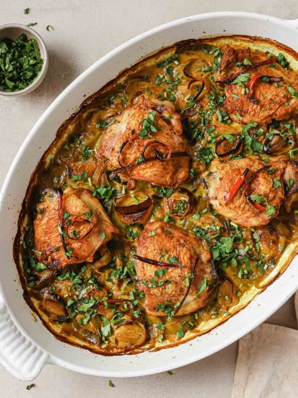 Image shows baked turmeric chicken thighs with leeks in a white casserole dish with dairy-free cream sauce.