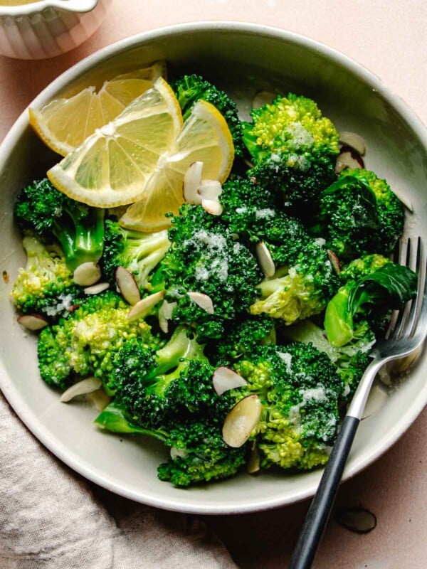 Image shows garlic butter ed broccoli served in a plate with lemon wedges on the side.