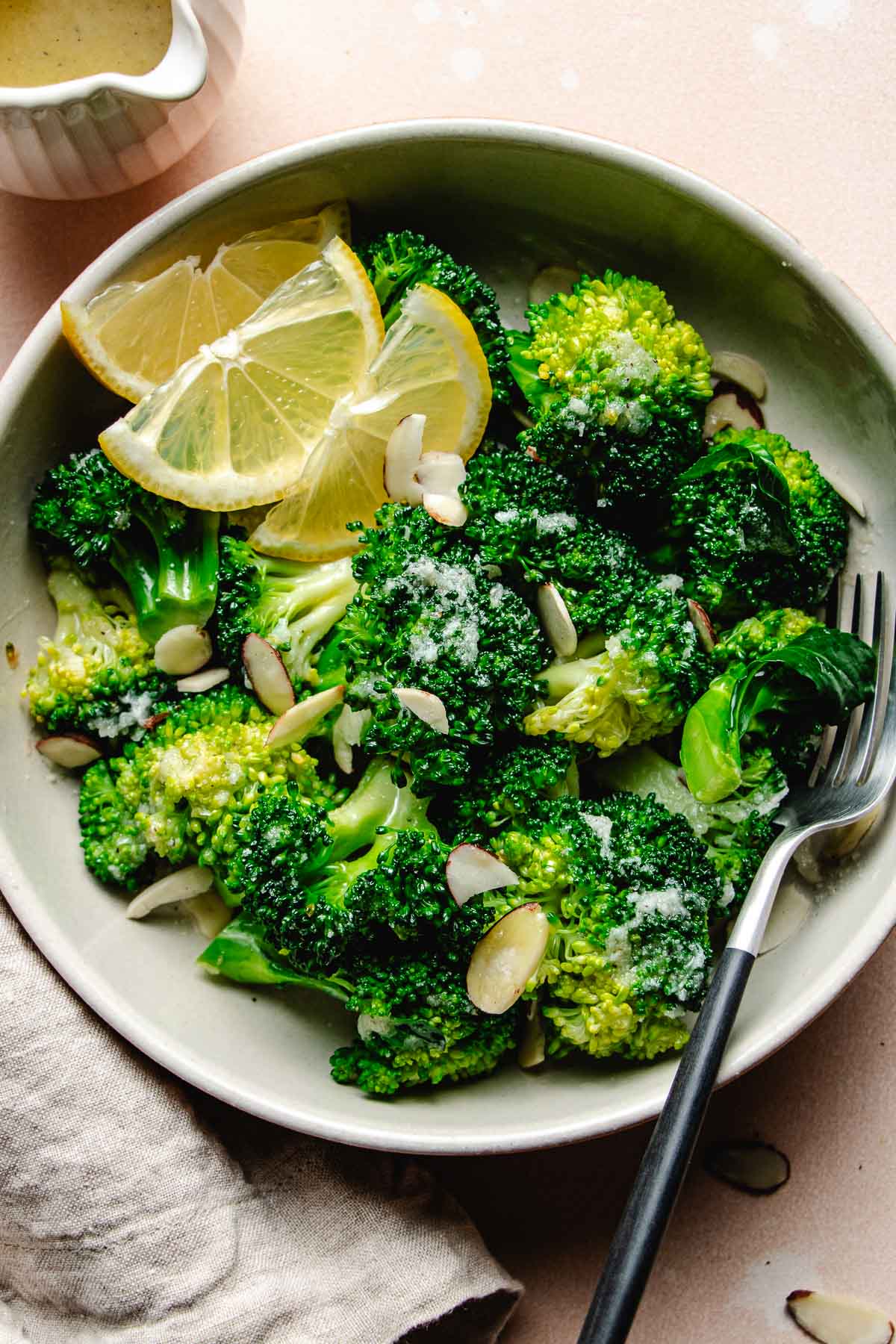 Image shows garlic butter ed broccoli served in a plate with lemon wedges on the side.