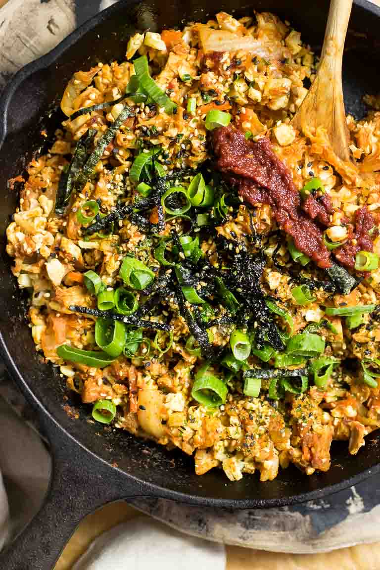 A cast iron skillet loaded with cauliflower fried rice, kimchi, and homemade gochujang sauce.