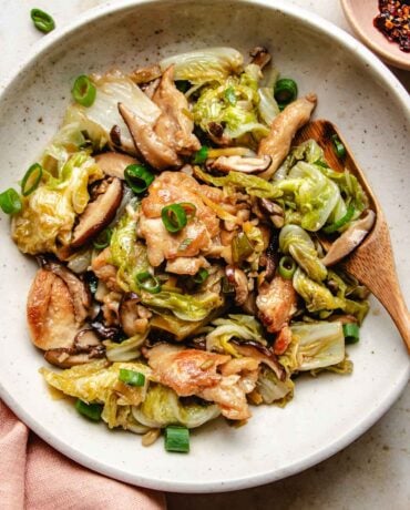 Image shows stir fried napa cabbage with chicken breasts and shiitake served on a white plate