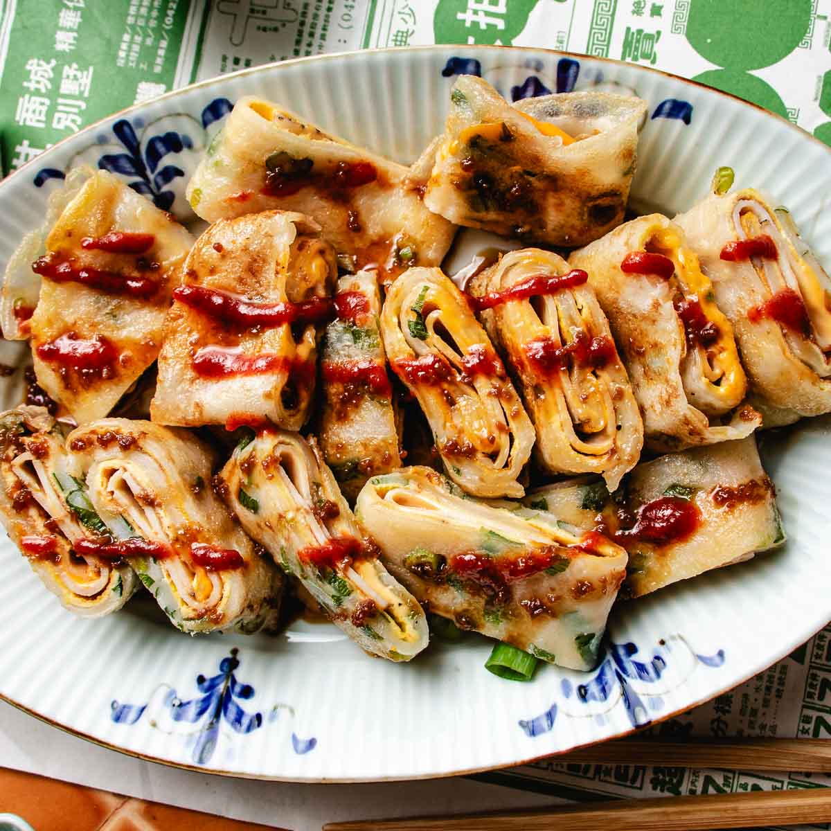 Recipe image of Dan Bing egg crepes with gooey cheese and savory ham stuffed inside, served over a plate.