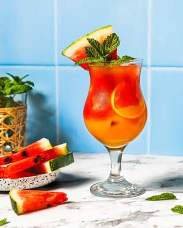 Feature image shows watermelon mocktail drinks non-alcoholic served in a glass with more watermelon on top for garnish.