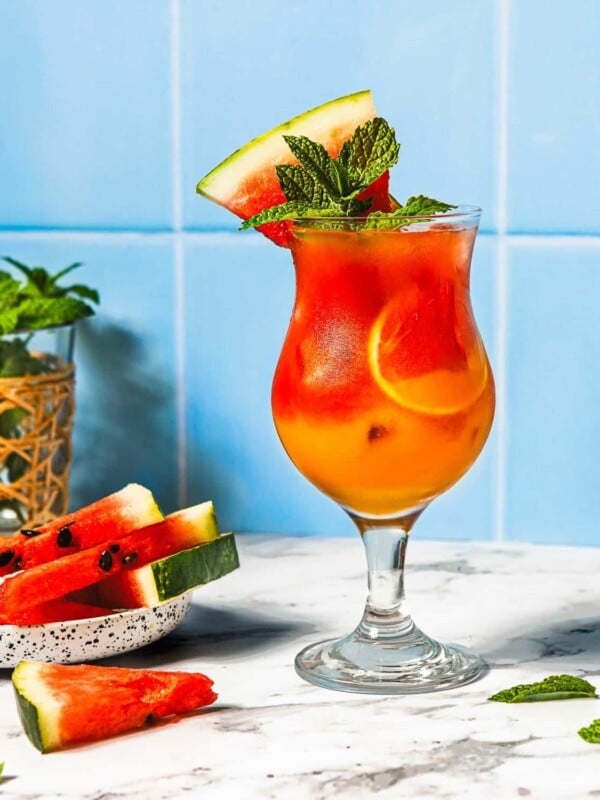 Feature image shows watermelon mocktail drinks non-alcoholic served in a glass with more watermelon on top for garnish.