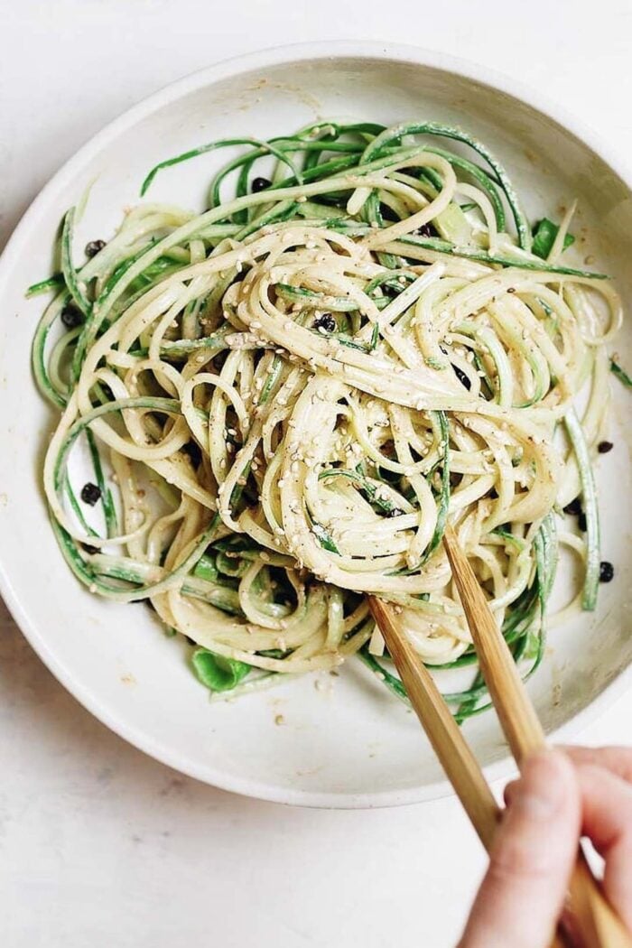 A close shot photo shows cucumber noodles drizzled with thai peanut sauce in a serving bowl