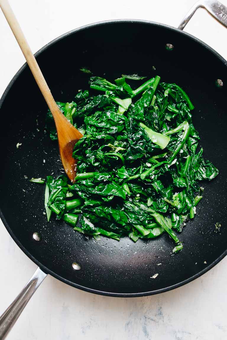 Photo shows Gai Lan Recipe stir-fried with garlic and oil in a big wok with a wooden stir-fry spoon.