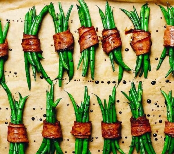 Photo shows baked bacon wrapped string beans over a lined sheet pan and drizzled with balsamic vinegar.