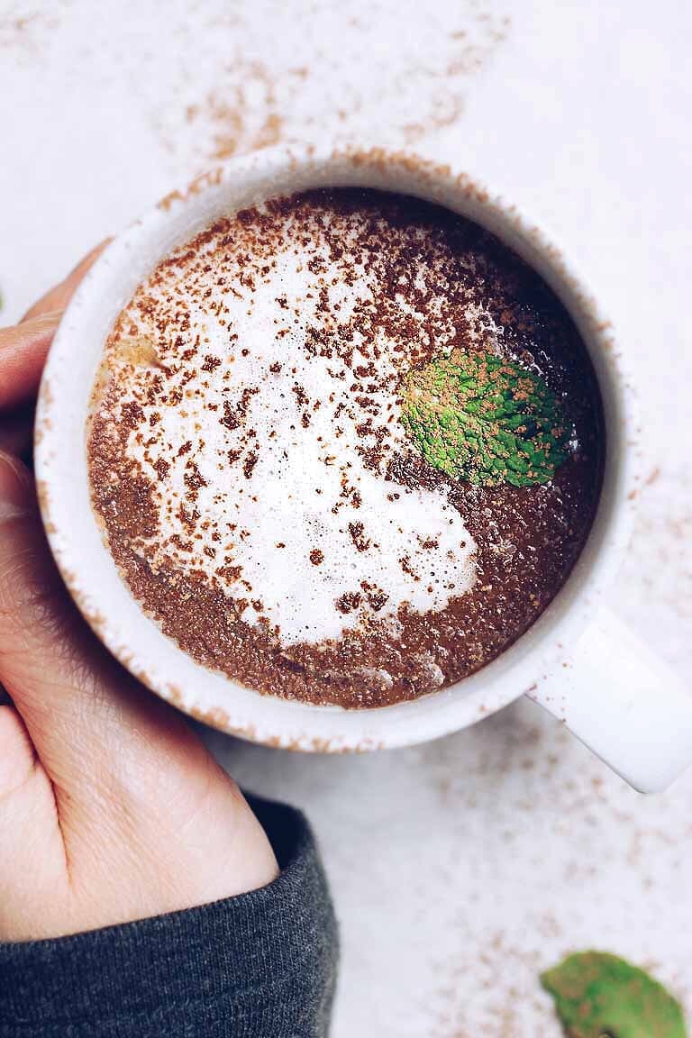 Feature image shows paleo hot chocolate served in a white mug with cocoa dusting in almond milk. 