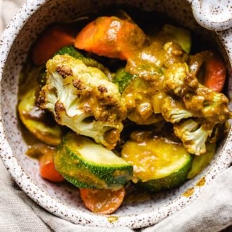 A close shot of photo shows roasted plant-based vegetables with curry sauce