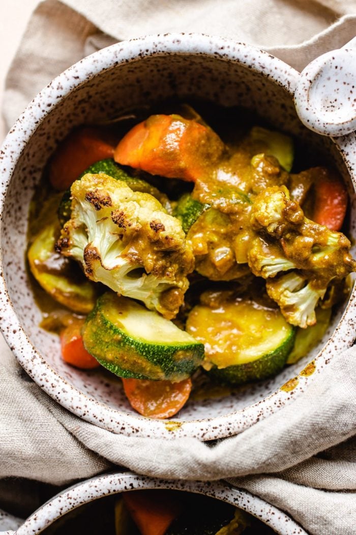 A close shot of photo shows roasted plant-based vegetables with curry sauce