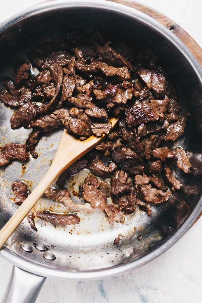 Man cooks meat in a frying pan. Hand using spatula to stir red and