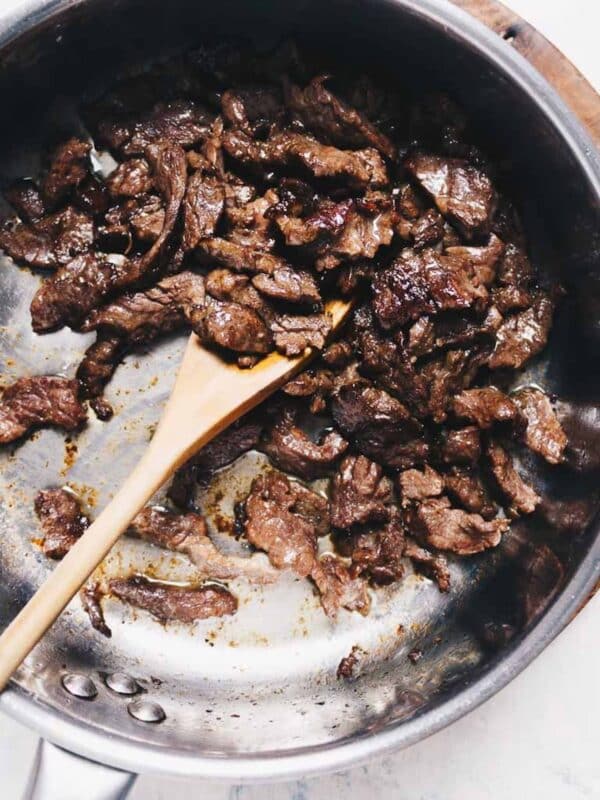 Slices of stir fried beef in a stainless steel pan, being stirred with a wooden spoon. The beef is browned, well-seasoned, and looks like the best velveted beef for stir fry—perfectly velvet beef for tender stir fry dishes.