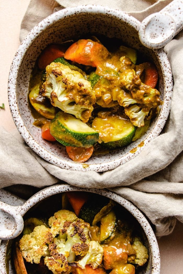 Photo shows two white bowls with roasted vegetable in curry sauce for plant-based dinner