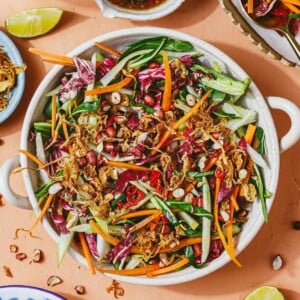 Recipe image shows a large plate of bok choy slaw with other freshly shredded vegetables, tossed in a nutty Thai chili lime dressing.