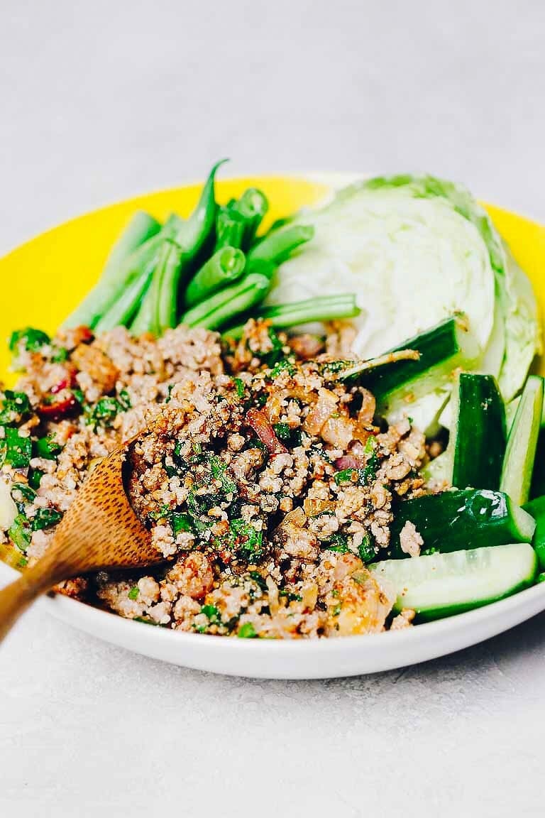 A side close shot shows laab moo (Thai pork larb) served with fresh vegetables in a yellow bowl with a spoon on the side.