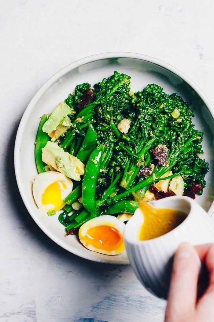 An overhead image shows pouring the Ginger dressing over blanched broccolini with avocado, eggs, and snow peas.