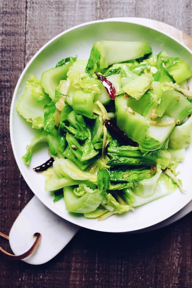 Chinese Mustard Greens sauteed with ginger and garlic with little chili peppers served on a white plate
