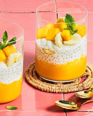 Image shows 2 glasswares filled with mango puree, sago pudding, and chopped mango and mint leaves served as a dessert.