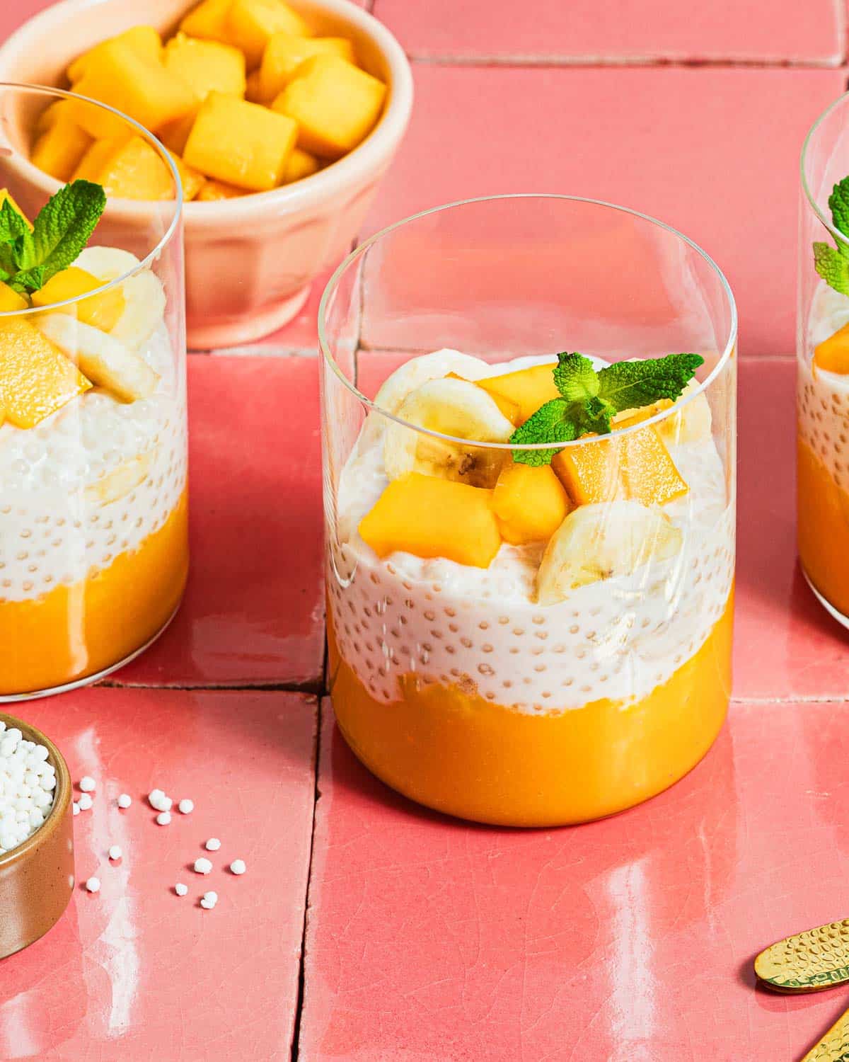 A close side shot shows sago pearls in coconut milk with mango in a glass jar.