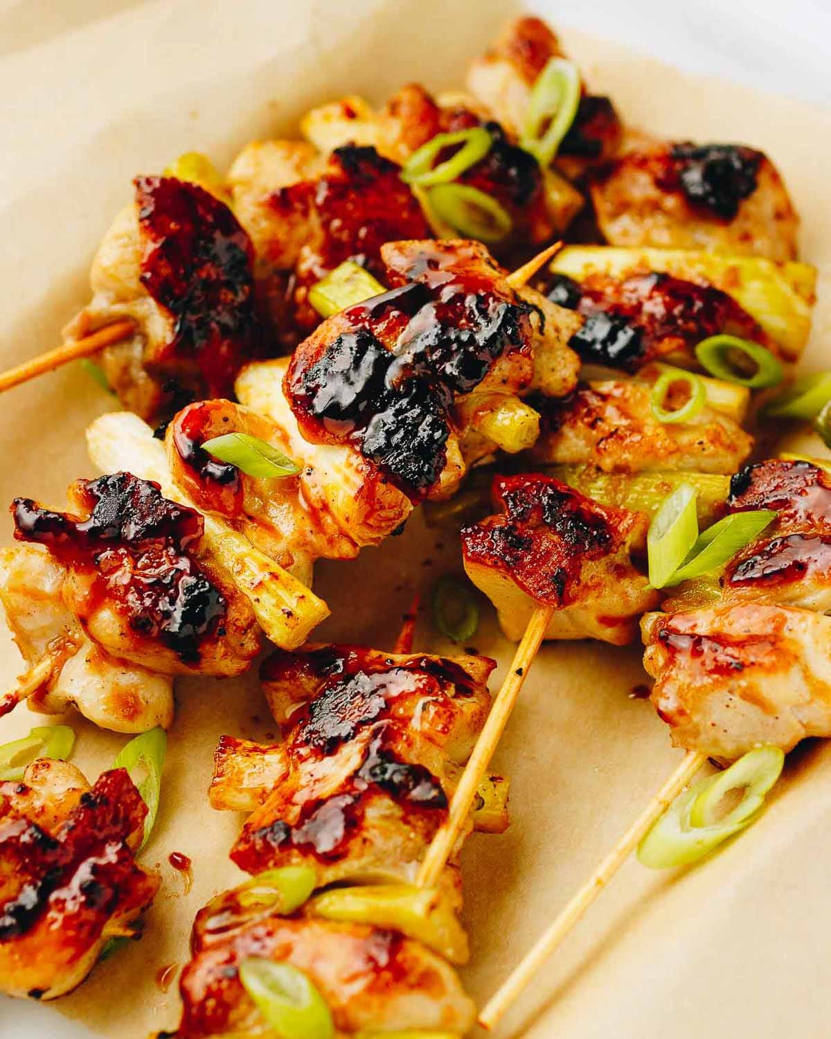 Grilled Negima Yakitori skewers glazed with a shiny, caramelized yakitori sauce, garnished with sliced green onions, served on parchment paper.