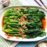 A plate of Chinese broccoli (gai lan) topped with chopped garlic and drizzled with soy sauce, served on a white dish with white rice and chopsticks nearby—an easy Chinese broccoli recipe perfect for any meal.