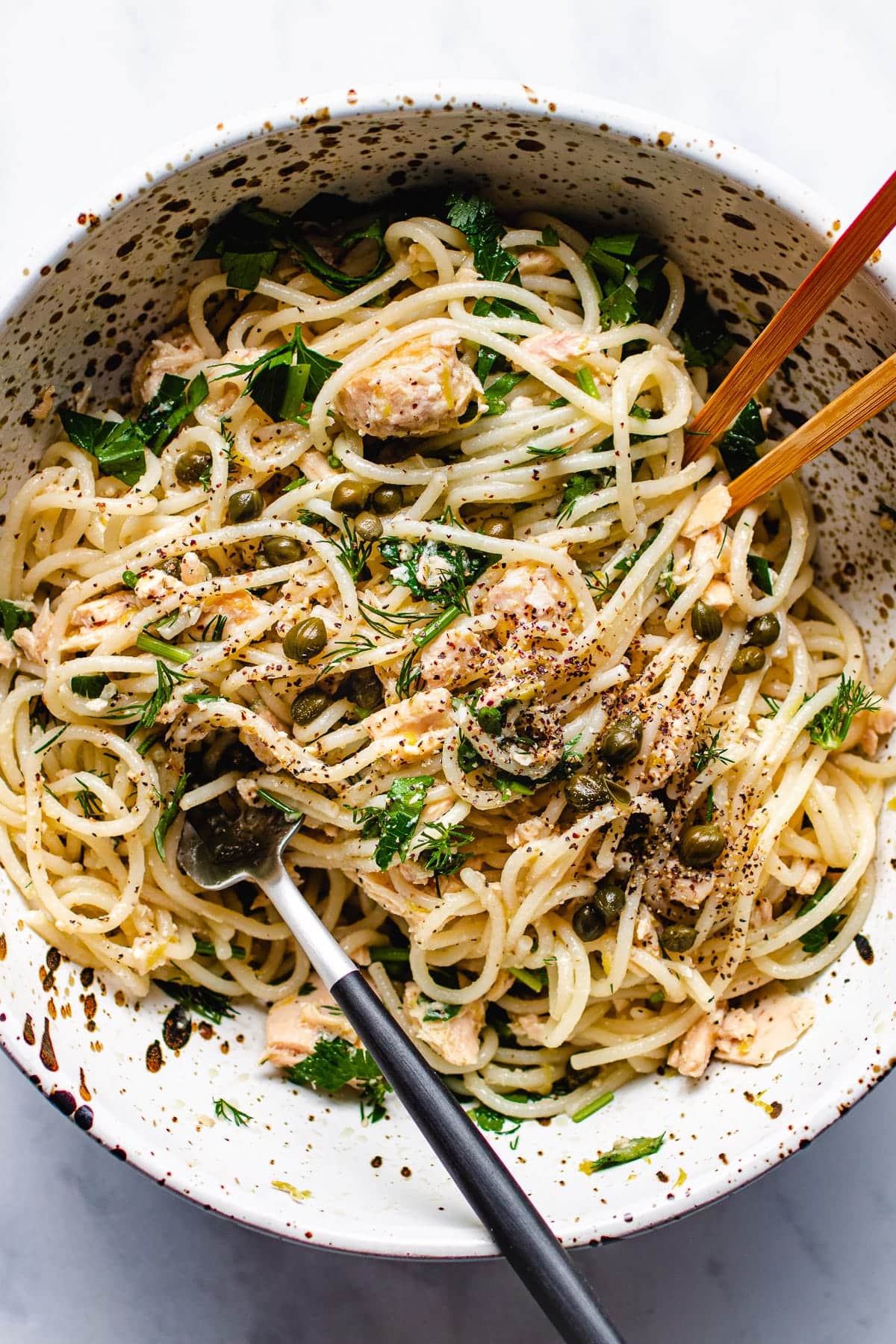 Photo shows a bowl of tuna spaghetti with fresh lemon zest, lemon juice, capers, and herbs tossed with spaghetti noodles in a large bowl.