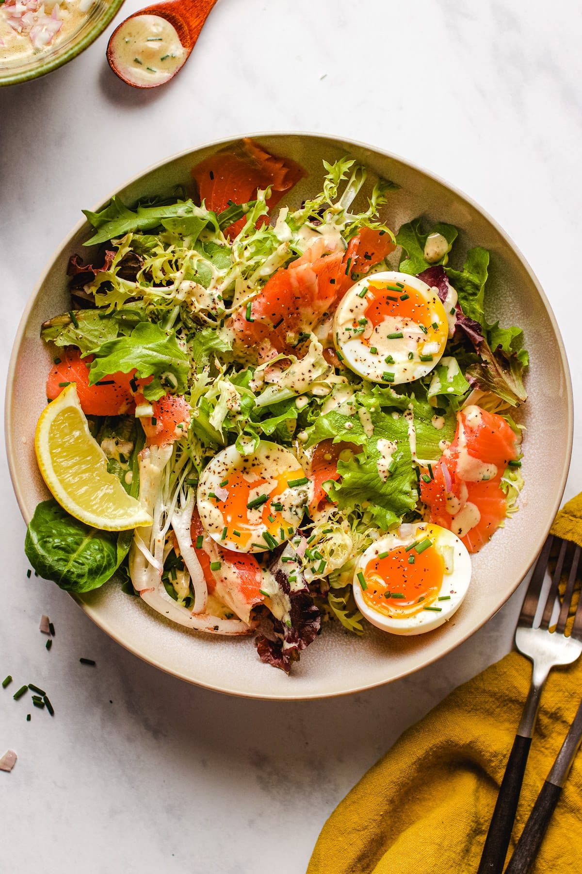 Feature image shows smoked salmon on a bed of crisp baby greens with soft boiled eggs and drizzled with caper chive dressing sauce.